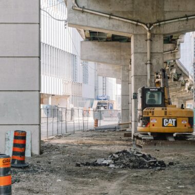 Site of roadway under concrete bridge construction with heavy equipment on dirty ground